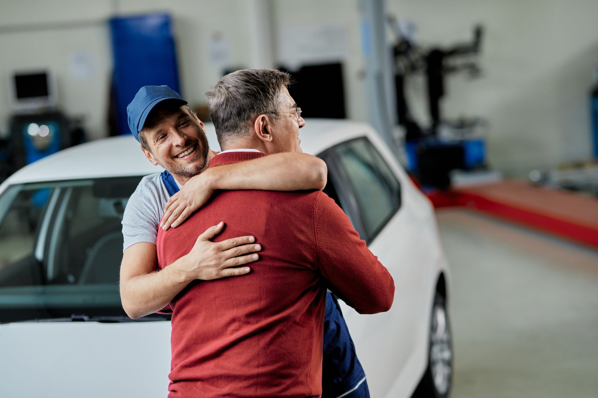 Happy mechanic and his customer greeting in auto repair shop.